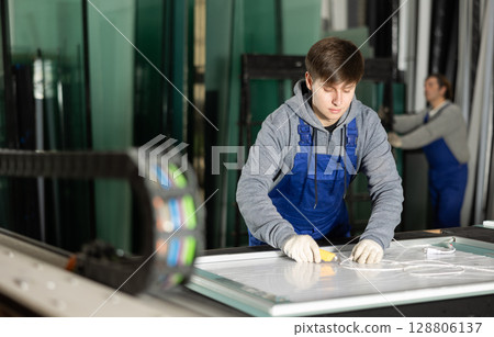 In workshop for production of glass products, guy co-worker cuts off excess from workpiece 128806137