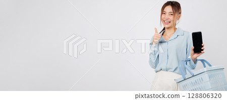 Shopping in supermarket, Asian woman holds basket and mobile phone screen show thumb up smiling and enjoying grocery shopping with cheerful online vibe. isolated studio white background 128806320