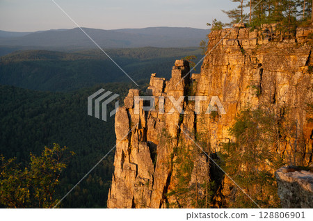 Scenic rocky cliff overlooking vast green valley at sunset in Ural Mountains Scenic rocky cliff overlooking vast green valley at sunset in Ural Mountains 128806901