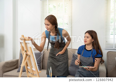 Lesbian artists collaborating on a canvas in a cozy living room Lesbian artists collaborating on a canvas in a cozy living room 128807942