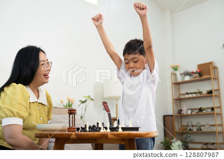 Joyful Learning. Child Celebrating Chess Victory with Grandmother at Home 128807987