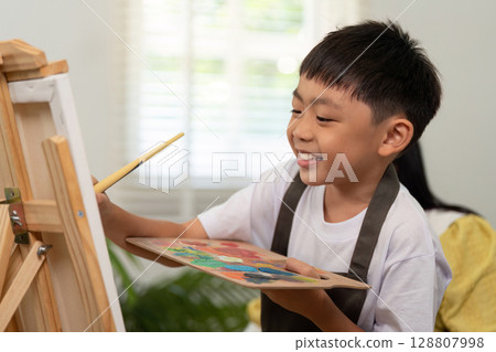 Creative Expression. Young boy painting on canvas with joy. Creative Expression. Young boy painting on canvas with joy. 128807998