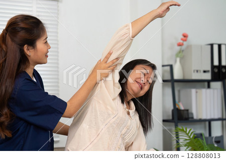 Caregiver helping elderly woman with stretching exercises at home 128808013