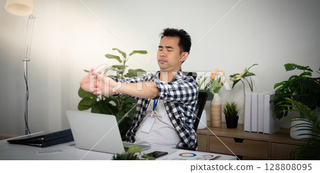Wellness. Young man stretching at his desk for better health and productivity. 128808095