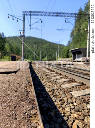 railway tracks leading to remote station surrounded by wilderness under clear blue sky. closeup. railway tracks leading to remote station surrounded by wilderness under clear blue sky. closeup. 128808231