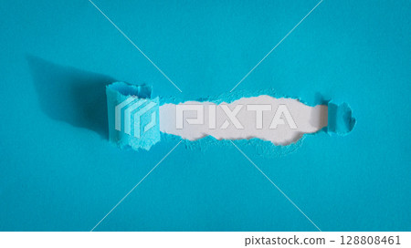 Hole ripped in blue paper on white background. 128808461