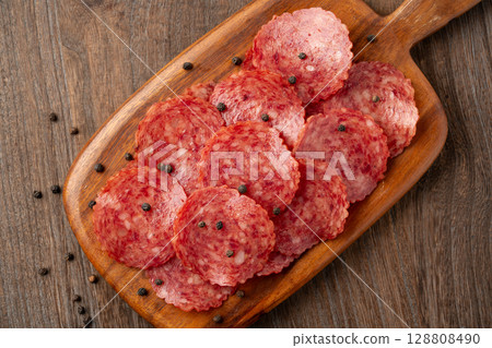 Delicious slices of salami on a wooden cutting board Delicious slices of salami on a wooden cutting board 128808490