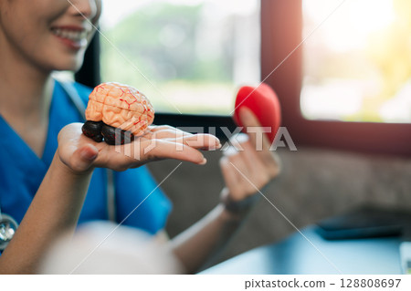 A healthcare worker in blue scrubs holds a brain model and heart symbol, symbolizing medical care and health education. A healthcare worker in blue scrubs holds a brain model and heart symbol, symbolizing medical care and health education. 128808697
