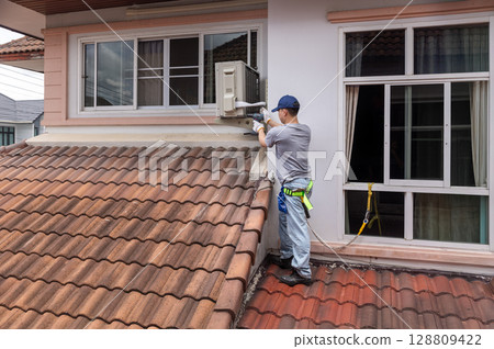 Technician  fixing air conditioner unit on outside wall. 128809422