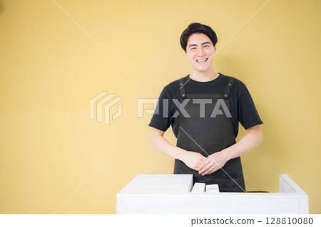 Image of a man wearing an apron for part-time work or customer service work, background yellow 128810080