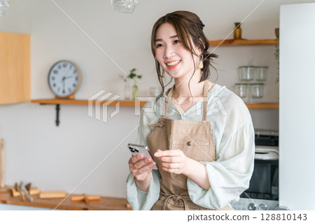 Asian woman using smartphone app in home kitchen/dining Asian woman using smartphone app in home kitchen/dining 128810143