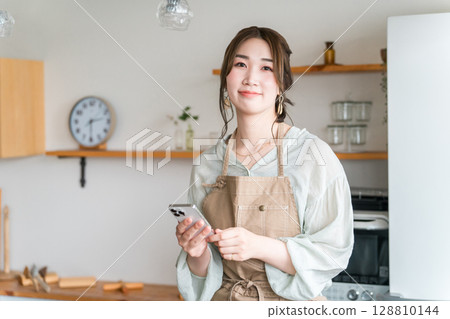 Asian woman using smartphone app in home kitchen/dining 128810144