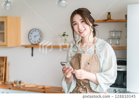 Asian woman using smartphone app in home kitchen/dining Asian woman using smartphone app in home kitchen/dining 128810145