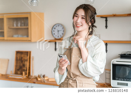 在家庭廚房/餐廳使用智能手機應用程序的亞洲女性 在家庭廚房/餐廳使用智能手機應用程序的亞洲女性 128810148