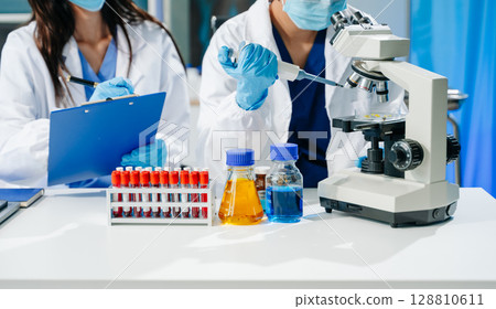 scientists in lab coats conducting research, handling glassware, and working with chemicals 128810611