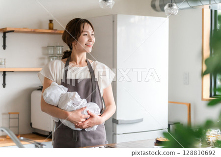 年輕的亞洲婦女在廚房裡抱著孩子 年輕的亞洲婦女在廚房裡抱著孩子 128810692