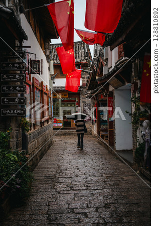 Tourists walking under umbrellas in Lijiang Old Town shopping street 128810892