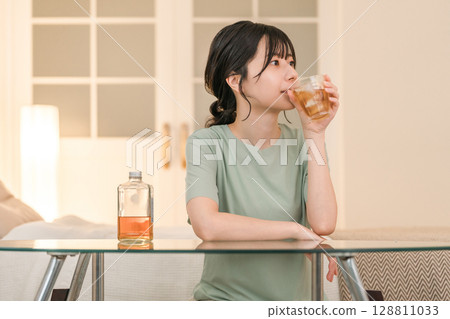 Young Asian woman having a drink in the bedroom at home (whisky, home drinking, drinking habits) 128811033