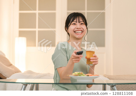 Young Asian woman laughing while watching TV and having a drink at dinner 128811108