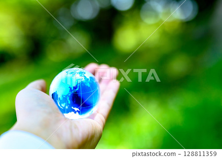 A crystal globe held up against beautiful new greenery - Ecology image - Clear, deep blue 128811359