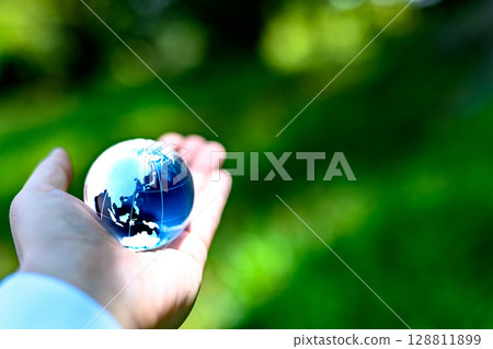 A crystal globe held up against beautiful new greenery - Ecological image - Metallic blue color A crystal globe held up against beautiful new greenery - Ecological image - Metallic blue color 128811899