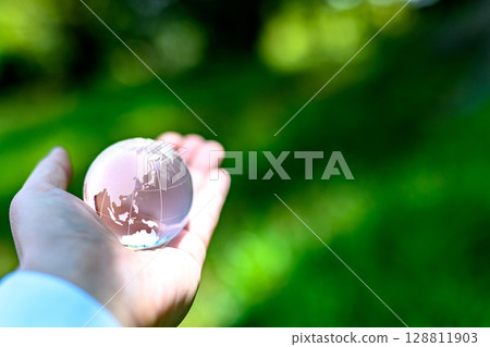 A crystal globe held up over beautiful new greenery - Ecology image - Normal color 128811903