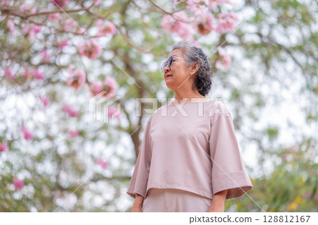 Elderly women with gray hair enjoying a beautiful moment together outdoors, surrounded by blooming pink flowers expressions reflect deep friendship and happiness relaxation with nature. 128812167
