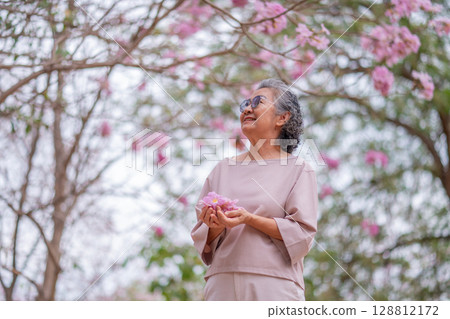 Elderly women with gray hair enjoying a beautiful moment together outdoors, surrounded by blooming pink flowers expressions reflect deep friendship and happiness relaxation with nature. Elderly women with gray hair enjoying a beautiful moment together outdoors, surrounded by blooming pink flowers expressions reflect deep friendship and happiness relaxation with nature. 128812172