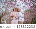 Elderly women with gray hair enjoying a beautiful moment together outdoors, surrounded by blooming pink flowers expressions reflect deep friendship and happiness relaxation with nature. 128812238