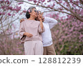 Elderly women with gray hair enjoying a beautiful moment together outdoors, surrounded by blooming pink flowers expressions reflect deep friendship and happiness relaxation with nature. 128812239