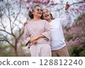 Elderly women with gray hair enjoying a beautiful moment together outdoors, surrounded by blooming pink flowers expressions reflect deep friendship and happiness relaxation with nature. 128812240