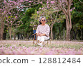 Elderly women with gray hair enjoying a beautiful moment together outdoors, surrounded by blooming pink flowers expressions reflect deep friendship and happiness relaxation with nature. 128812484