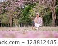 Elderly women with gray hair enjoying a beautiful moment together outdoors, surrounded by blooming pink flowers expressions reflect deep friendship and happiness relaxation with nature. 128812485