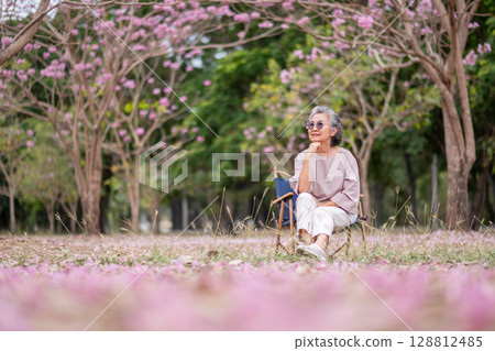 Elderly women with gray hair enjoying a beautiful moment together outdoors, surrounded by blooming pink flowers expressions reflect deep friendship and happiness relaxation with nature. Elderly women with gray hair enjoying a beautiful moment together outdoors, surrounded by blooming pink flowers expressions reflect deep friendship and happiness relaxation with nature. 128812485