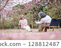 Elderly women with gray hair enjoying a beautiful moment together outdoors, surrounded by blooming pink flowers expressions reflect deep friendship and happiness relaxation with nature. 128812487
