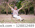 Elderly women with gray hair enjoying a beautiful moment together outdoors, surrounded by blooming pink flowers expressions reflect deep friendship and happiness relaxation with nature. 128812489