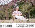Elderly women with gray hair enjoying a beautiful moment together outdoors, surrounded by blooming pink flowers expressions reflect deep friendship and happiness relaxation with nature. 128812490