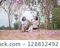 Elderly women with gray hair enjoying a beautiful moment together outdoors, surrounded by blooming pink flowers expressions reflect deep friendship and happiness relaxation with nature. 128812492