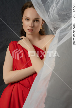 Woman poses in elegant red gown against dramatic studio backdrop, conveying a range of emotions and expressions Woman poses in elegant red gown against dramatic studio backdrop, conveying a range of emotions and expressions 128812720