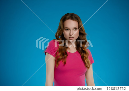 Woman with long hair poses emotionally in a studio setting against a blue background, showcasing confidence and charm in her expression 128812732