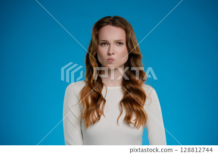 Woman expressing a thoughtful emotion while posing in a studio with a blue background 128812744