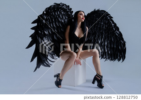 Woman in black lingerie with striking wings poses elegantly in a studio setting 128812750