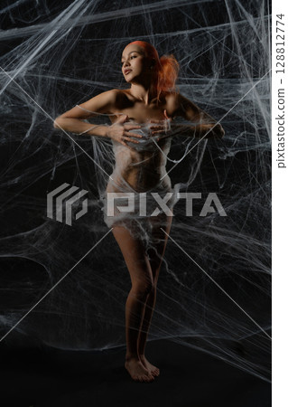 Woman with red hair caught in a delicate net trap against a dark backdrop 128812774