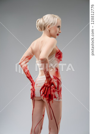 Naked woman covered in blood body art poses in a studio setting 128812776