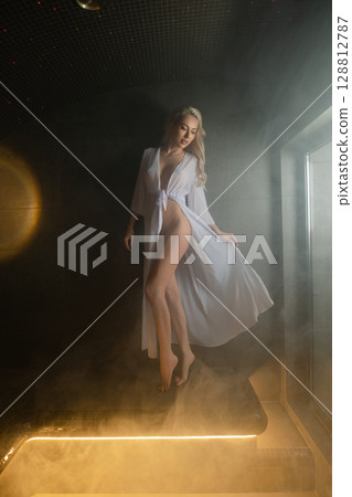 Woman in a white robe relaxes in a calming sauna atmosphere Woman in a white robe relaxes in a calming sauna atmosphere 128812787