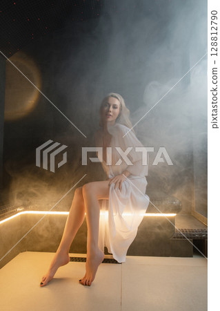 Woman enjoys relaxation in a peaceful sauna with soft lighting and steam 128812790