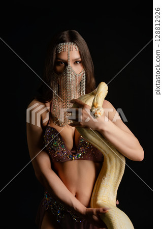 Woman poses gracefully with a snake in a captivating studio setting Woman poses gracefully with a snake in a captivating studio setting 128812926
