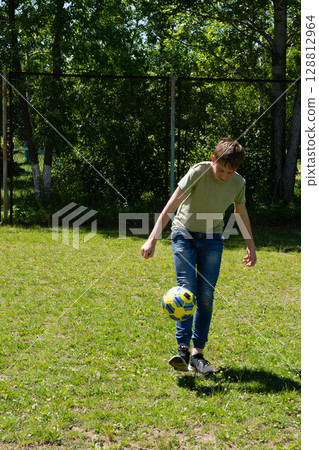 Boy juggles soccer ball on grassy field, sunny day. 128812964