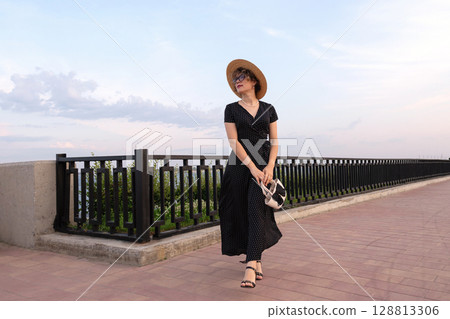 Woman walks in polka dot dress along riverside walkway Woman walks in polka dot dress along riverside walkway 128813306