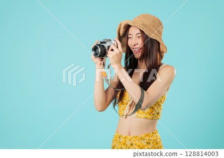 Happy young Asian woman tourist holding camera reviewing the photo on screen, for her travel memories she smiles as she gets ready to travel again, headshots isolated studio blue background 128814003